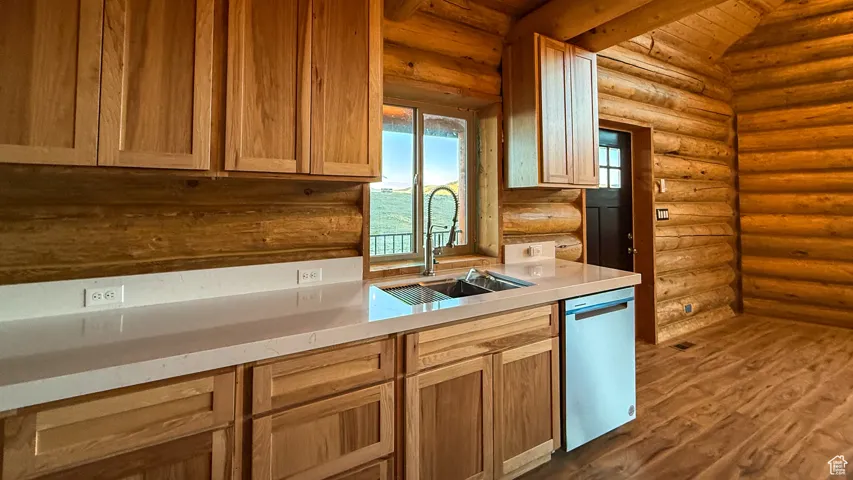 Kitchen with dark wood finished floors, log walls, light countertops, dishwasher, and beamed ceiling