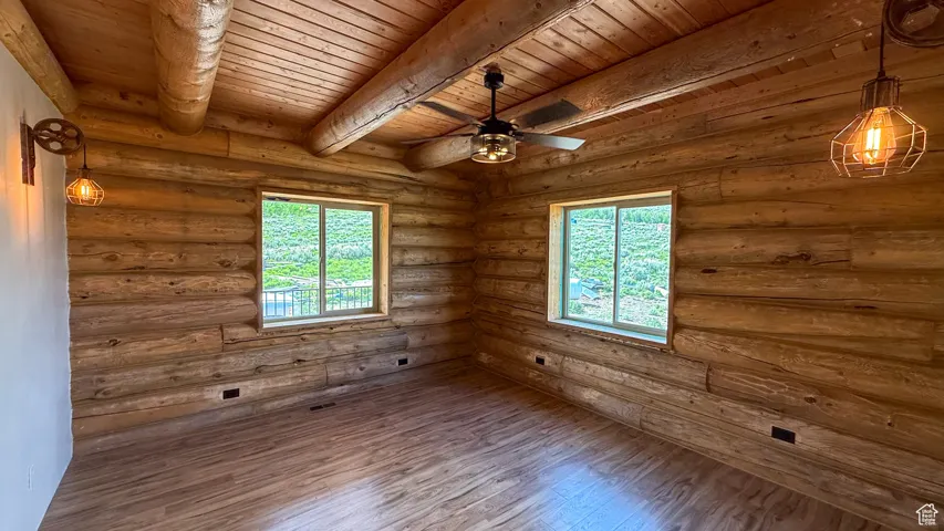Unfurnished room with wood ceiling with exposed beams, wood finished floors, ceiling fan, and log walls