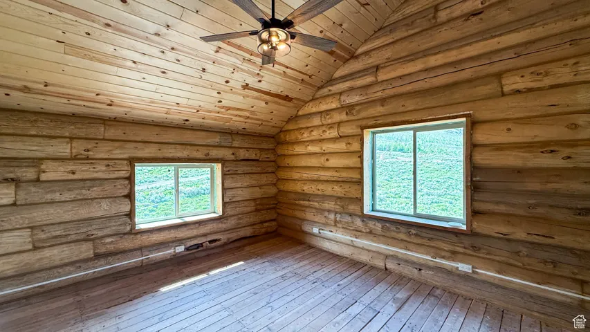 Vaulted ceiling bedroom with high ceilings and picture windows with views and natural light.   Featuring ceiling fan, hardwood / wood-style floors, healthy amount of natural light, lofted ceiling, and rustic walls