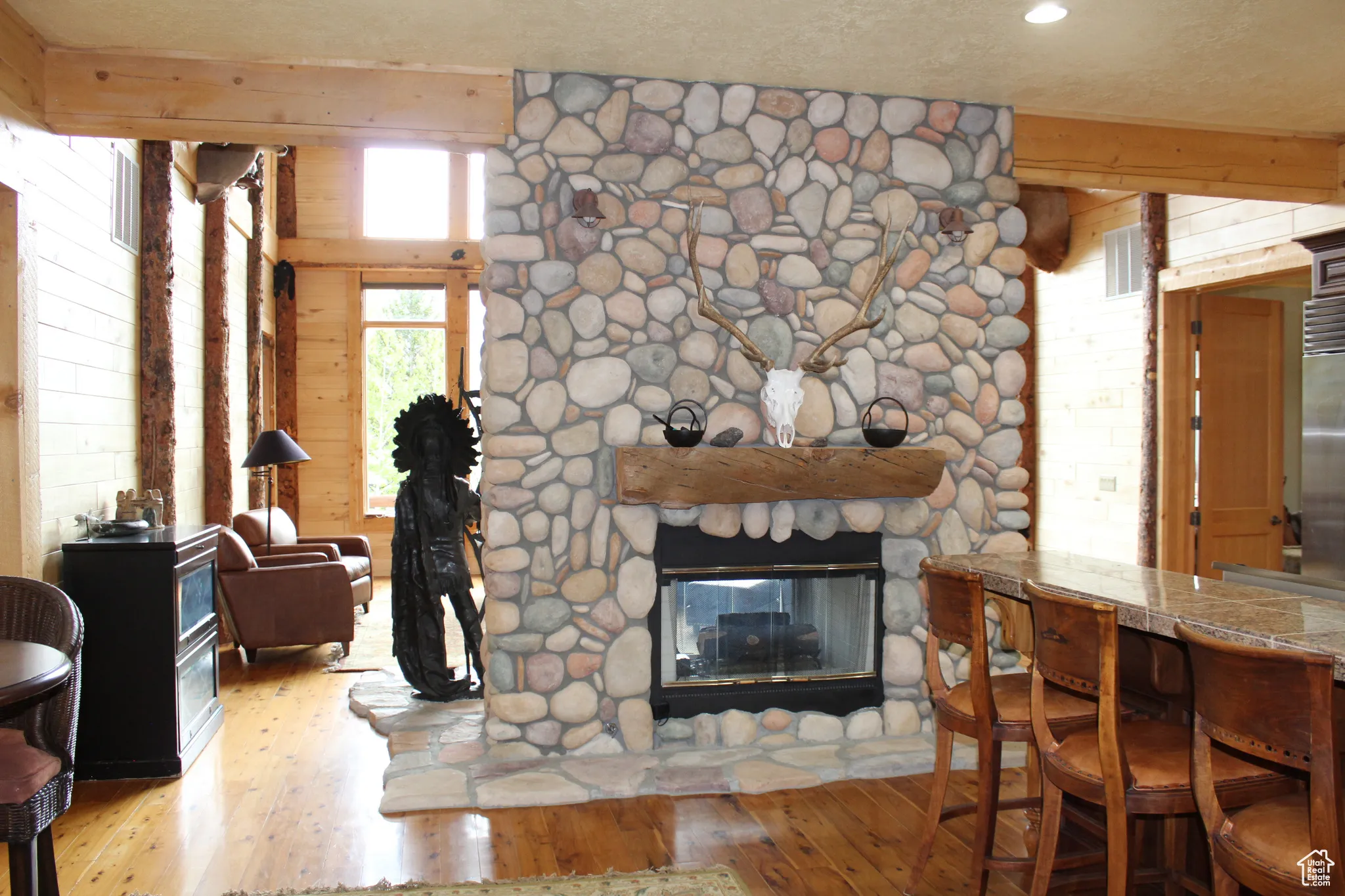 Living room featuring wood-type flooring, a stone fireplace, and wooden walls