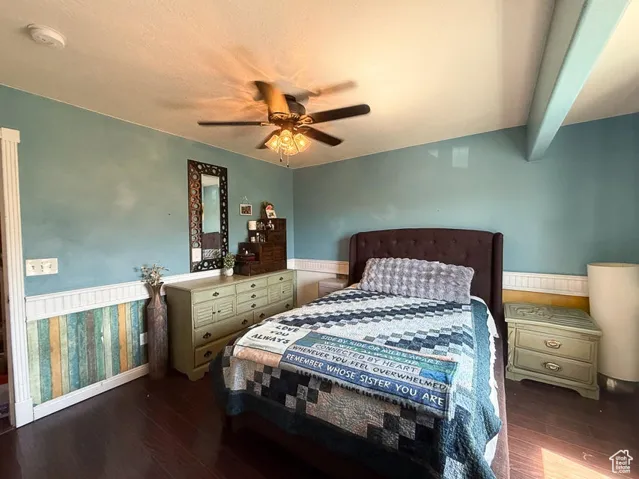 Bedroom featuring wood finished floors, baseboards, a ceiling fan, and a wainscoted wall