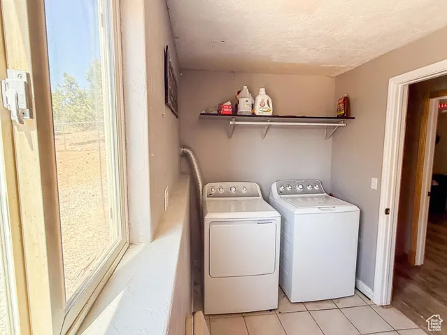 Washroom with washing machine and clothes dryer, light tile patterned floors, and a textured ceiling