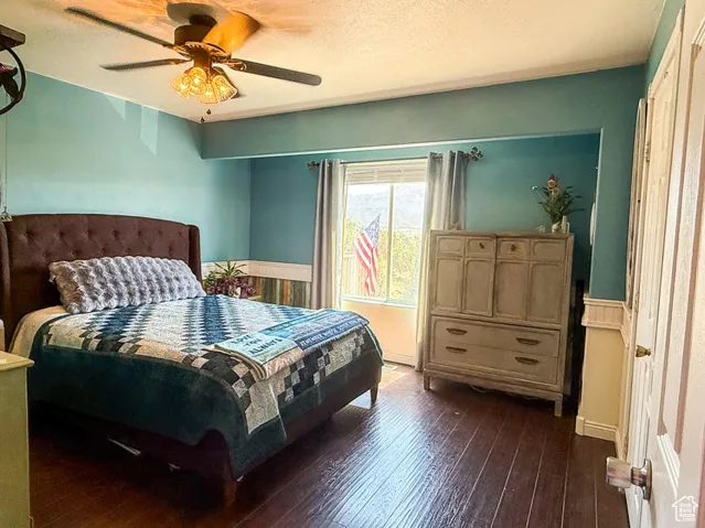Bedroom featuring dark wood finished floors, a ceiling fan, and a wainscoted wall