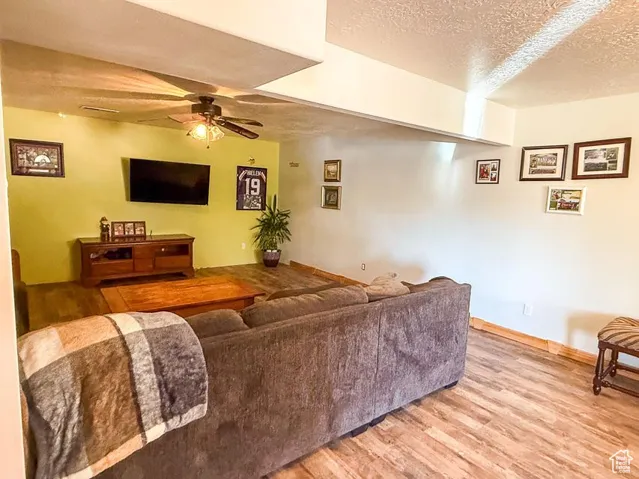 Living room with a textured ceiling, light wood-style flooring, ceiling fan, and baseboards