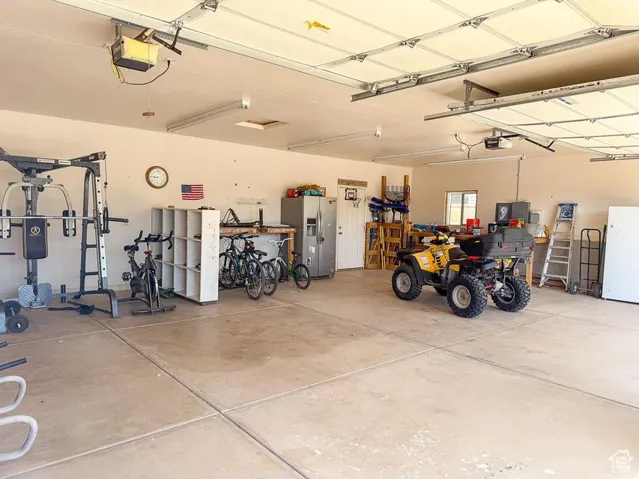 Garage featuring stainless steel fridge, a garage door opener, and freestanding refrigerator