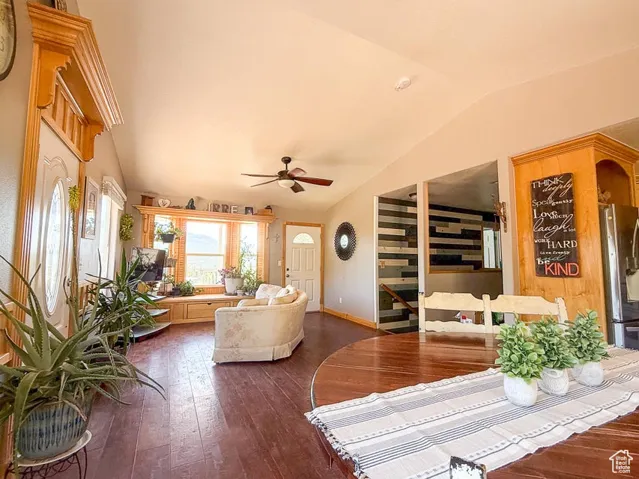 Living room with vaulted ceiling, dark wood-style floors, a ceiling fan, and baseboards