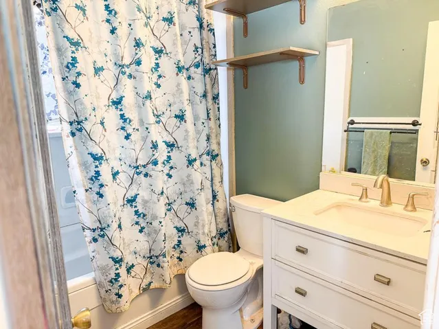 Full bath featuring toilet, vanity, shower / bath combination with curtain, and wood finished floors