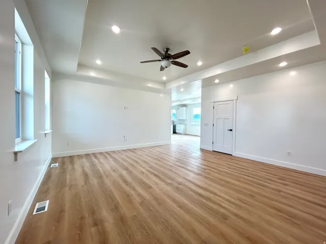 Unfurnished living room featuring a tray ceiling, ceiling fan, light wood-style floors, recessed lighting, and a fireplace