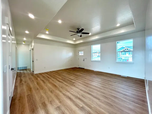 Unfurnished room featuring a raised ceiling, light wood finished floors, ceiling fan, and recessed lighting
