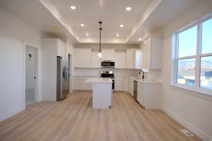 Kitchen with a kitchen island, white cabinetry, hanging light fixtures, appliances with stainless steel finishes, and decorative backsplash