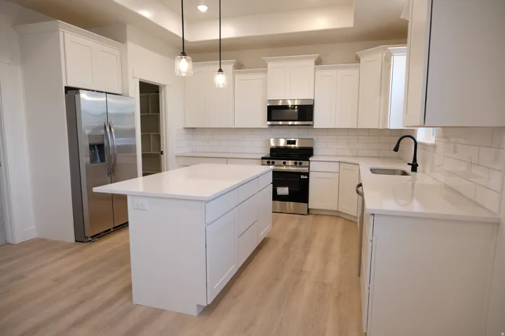 Kitchen with appliances with stainless steel finishes, decorative light fixtures, white cabinetry, a kitchen island, and backsplash