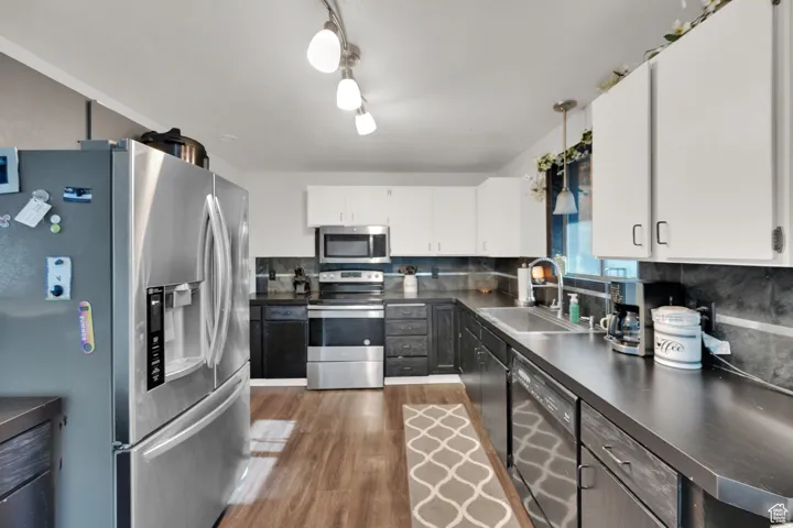 Kitchen with appliances with stainless steel finishes, a sink, dark countertops, wood finished floors, and white cabinetry