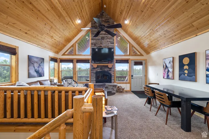 Living room with a stone fireplace, carpet flooring, high vaulted ceiling, wooden ceiling, and a ceiling fan