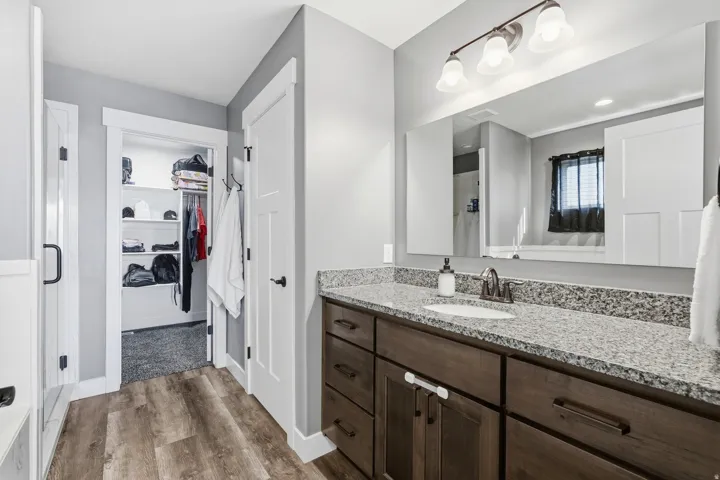 Wood-finish flooring, dark wood cabinetry with brushed nickel hardware, light granite countertop, built-in medicine cabinet, and recessed overhead lighting