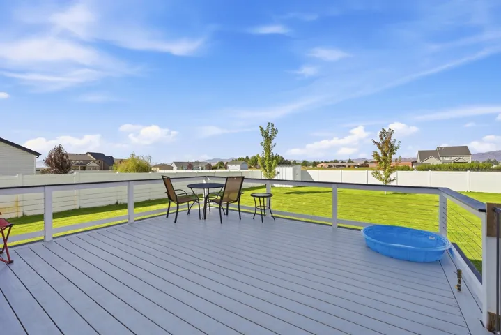 Expansive outdoor deck with gray composite decking and cable railing, overlooking a sizable green lawn enclosed by a white privacy fence