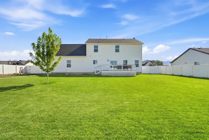 Expansive green lawn, white privacy fencing, rear deck, white siding, and a dark shingle roof