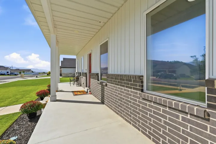 Concrete front porch with white columns, vertical siding, brick facade, and large windows