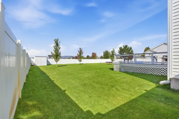 Expansive lawn area with a perimeter fence, a raised deck featuring latticework, and established trees