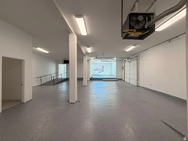 Spacious interior featuring a gray speckled floor, multiple fluorescent light fixtures, two white garage doors, and a built-in ramp