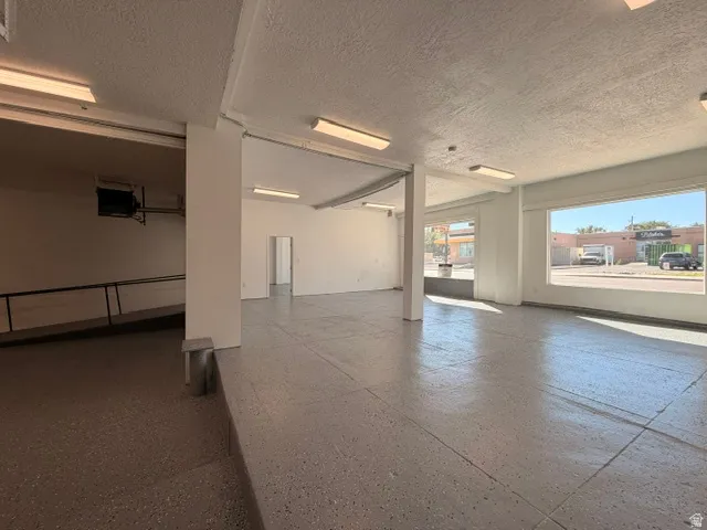 Expansive open-concept space featuring large storefront windows, uniform flooring, exposed ceiling, and integrated fluorescent lighting
