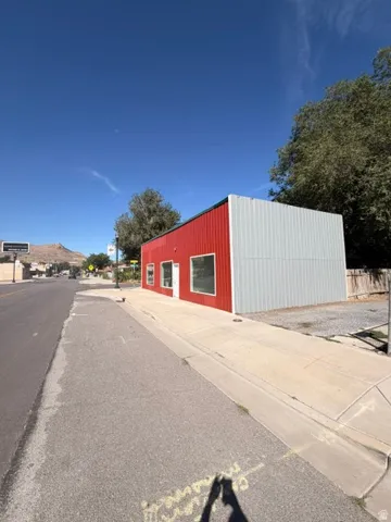 Commercial structure featuring a red and grey corrugated metal exterior, multiple window openings, and a prominent pedestrian sidewalk