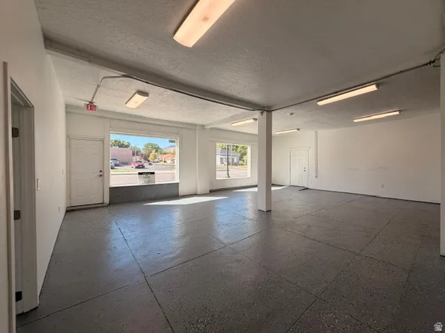 Open-concept commercial space featuring expansive windows, exposed beam ceiling, column supports, durable flooring, and multiple fluorescent lighting fixtures