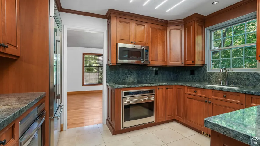 Kitchen with appliances with stainless steel finishes, brown cabinets, decorative backsplash, crown molding, and light tile patterned floors