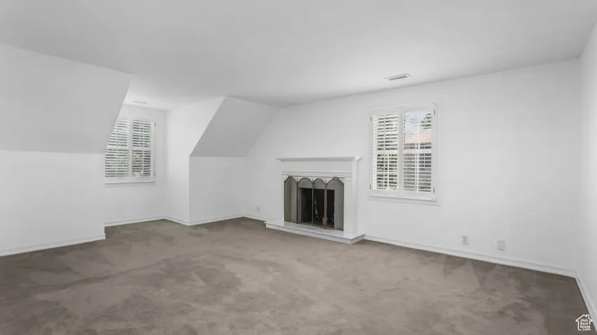 Unfurnished living room featuring carpet and a fireplace with raised hearth