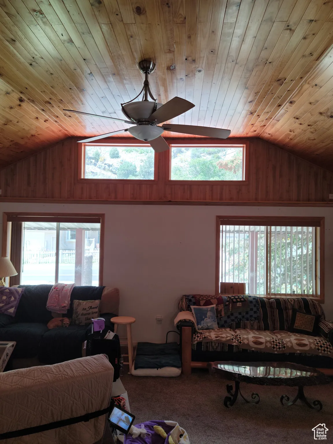 Carpeted living room featuring wood ceiling, a ceiling fan, wooden walls, and high vaulted ceiling