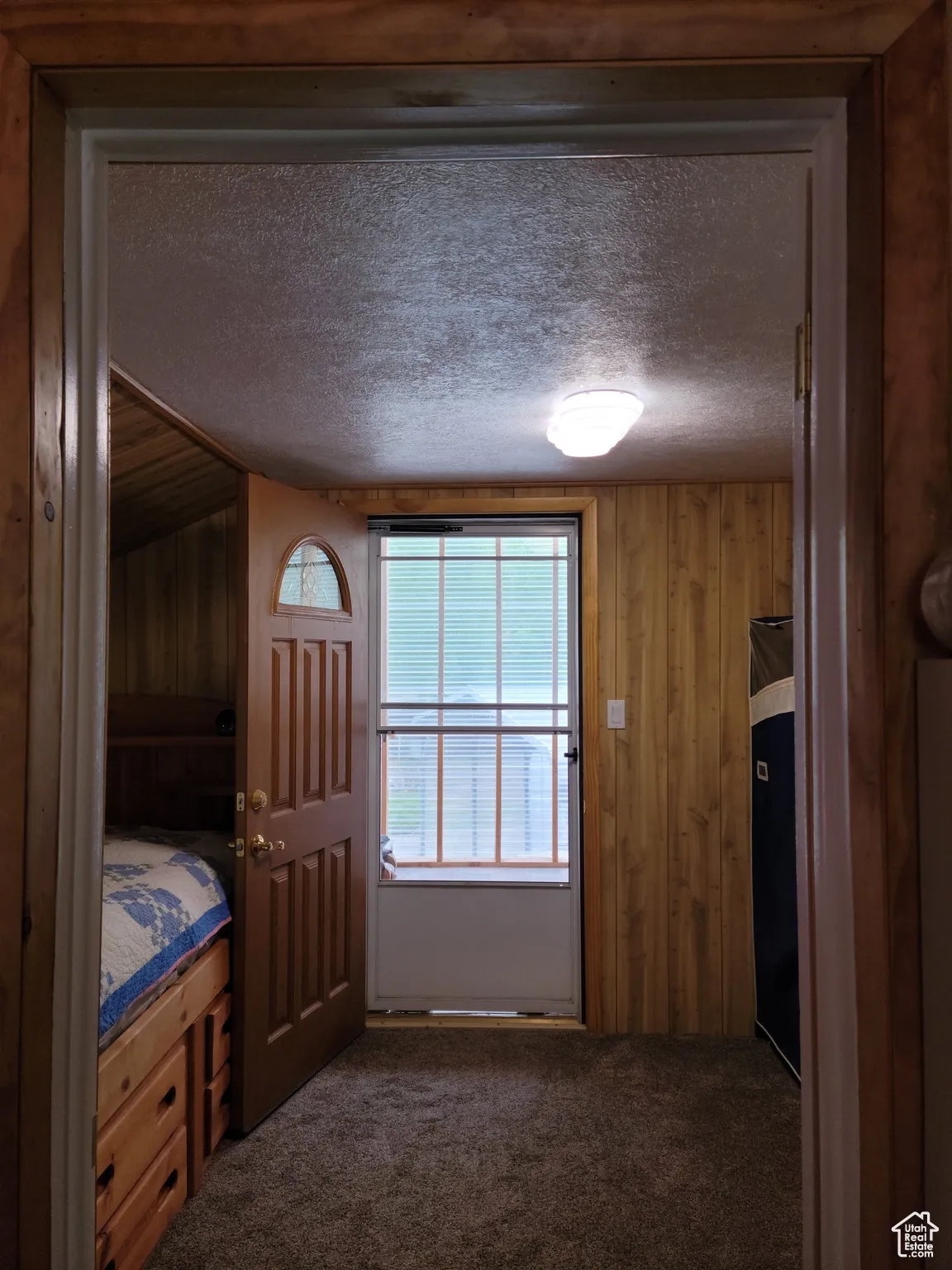 Bedroom featuring a textured ceiling, dark colored carpet, and wooden walls