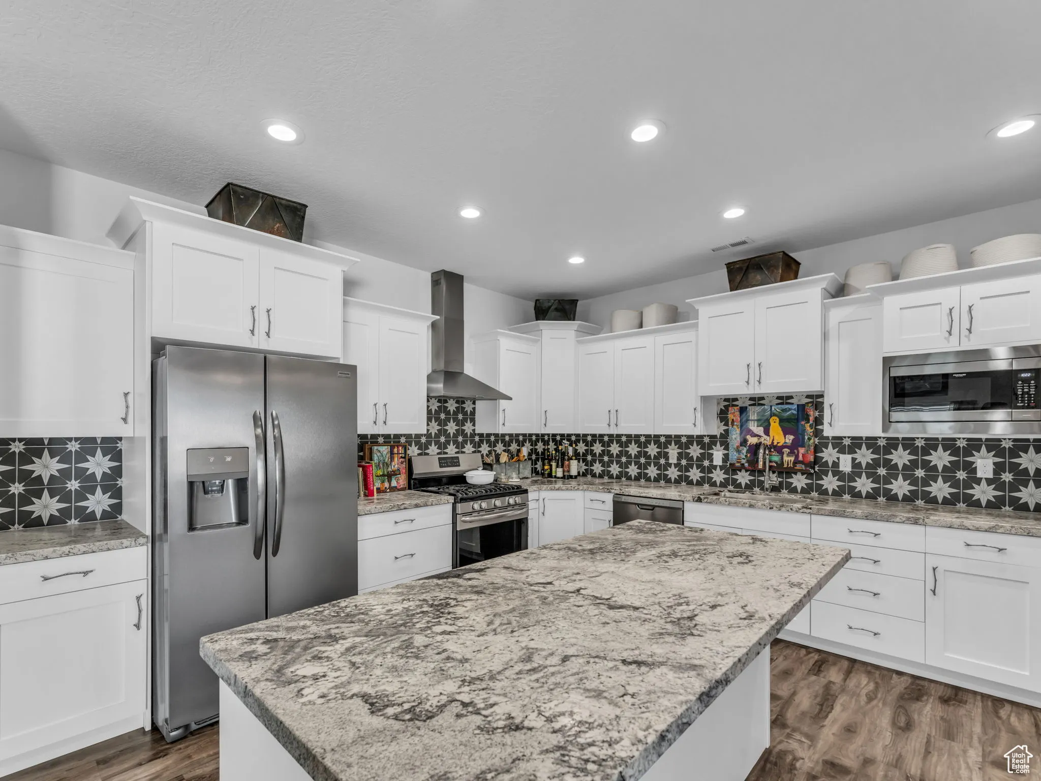 Kitchen featuring stainless steel appliances, wall chimney range hood, white cabinets, a kitchen island, and recessed lighting