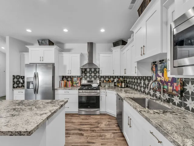 Kitchen with stainless steel appliances, wall chimney exhaust hood, dark wood-style flooring, decorative backsplash, and recessed lighting