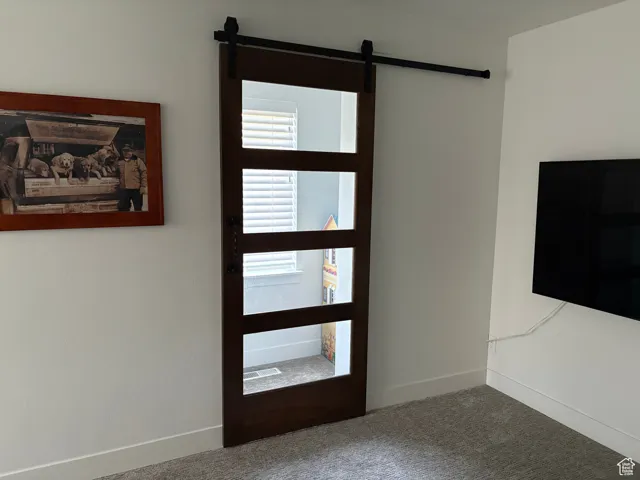 Carpeted entryway featuring a barn door and baseboards