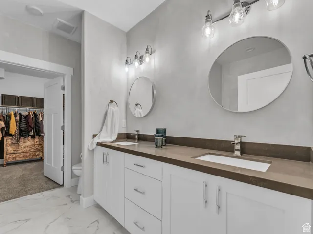 Bathroom featuring double vanity, marble finish flooring, and a spacious closet