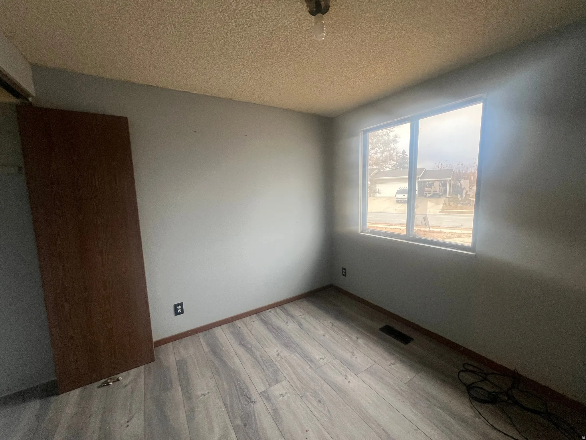 Empty room with light wood-style floors and a textured ceiling