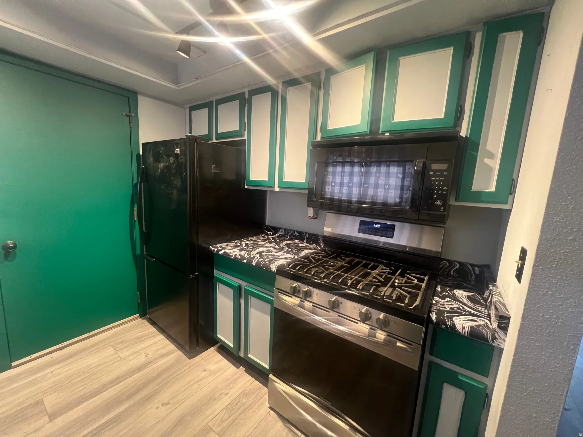 Kitchen featuring green cabinetry, black appliances, light wood-style flooring, glass insert cabinets, and white cabinets