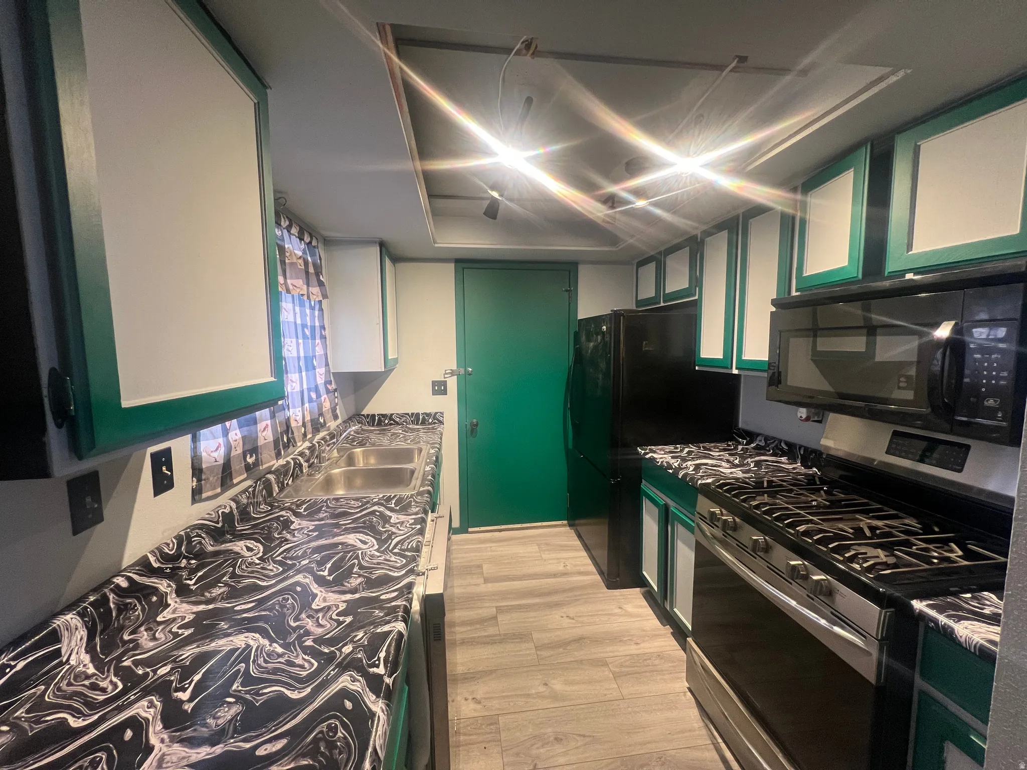 Kitchen with green cabinetry, black appliances, glass insert cabinets, and light wood-style floors