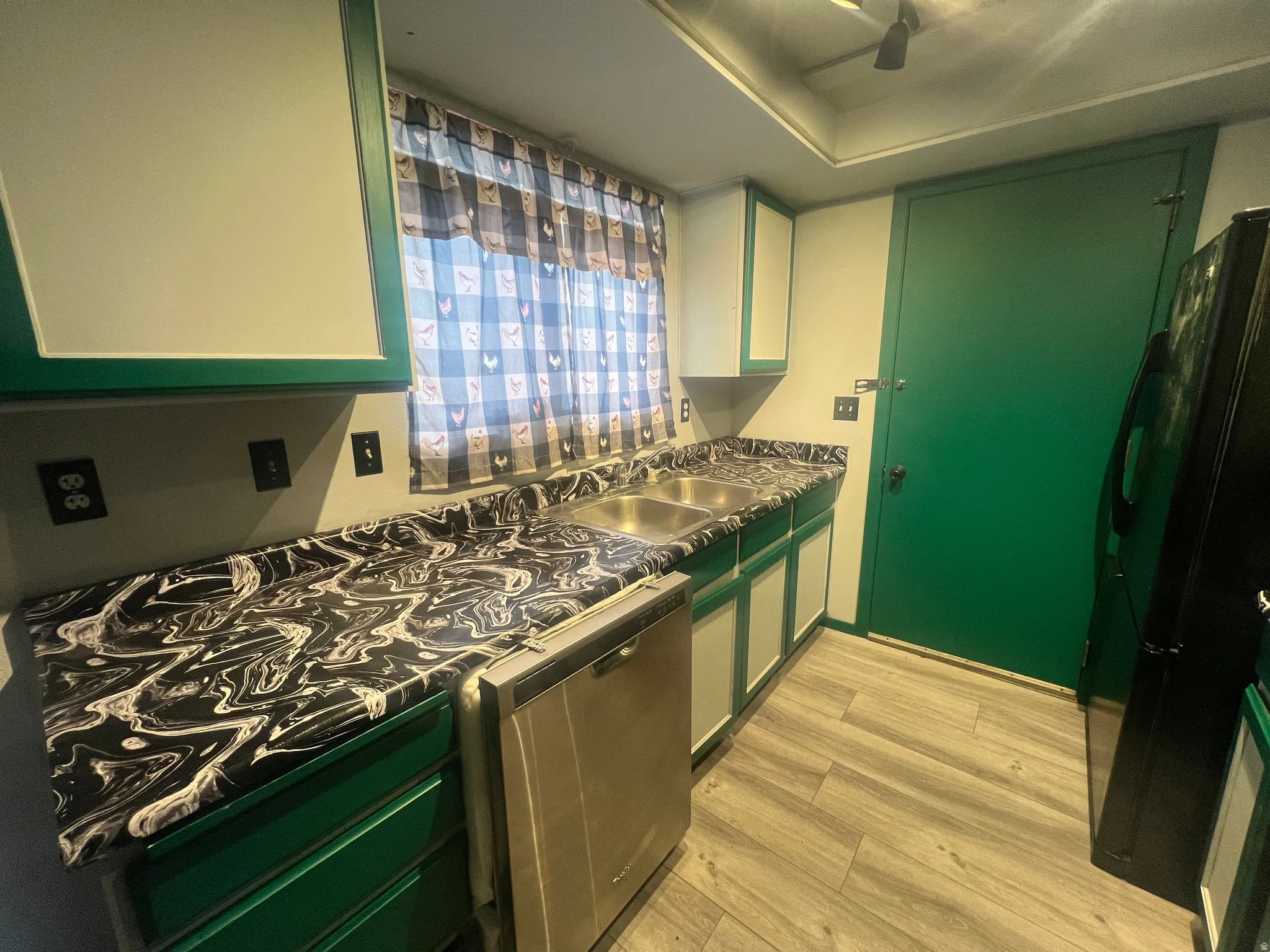 Kitchen with green cabinets, dark countertops, stainless steel appliances, and light wood-type flooring