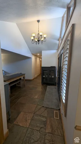 Hall featuring stone tile flooring, lofted ceiling, and a chandelier