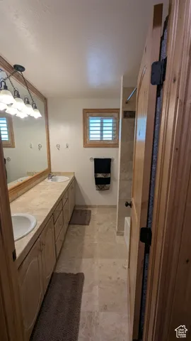 Full bathroom with double vanity, healthy amount of natural light, stone finish flooring, and a textured ceiling
