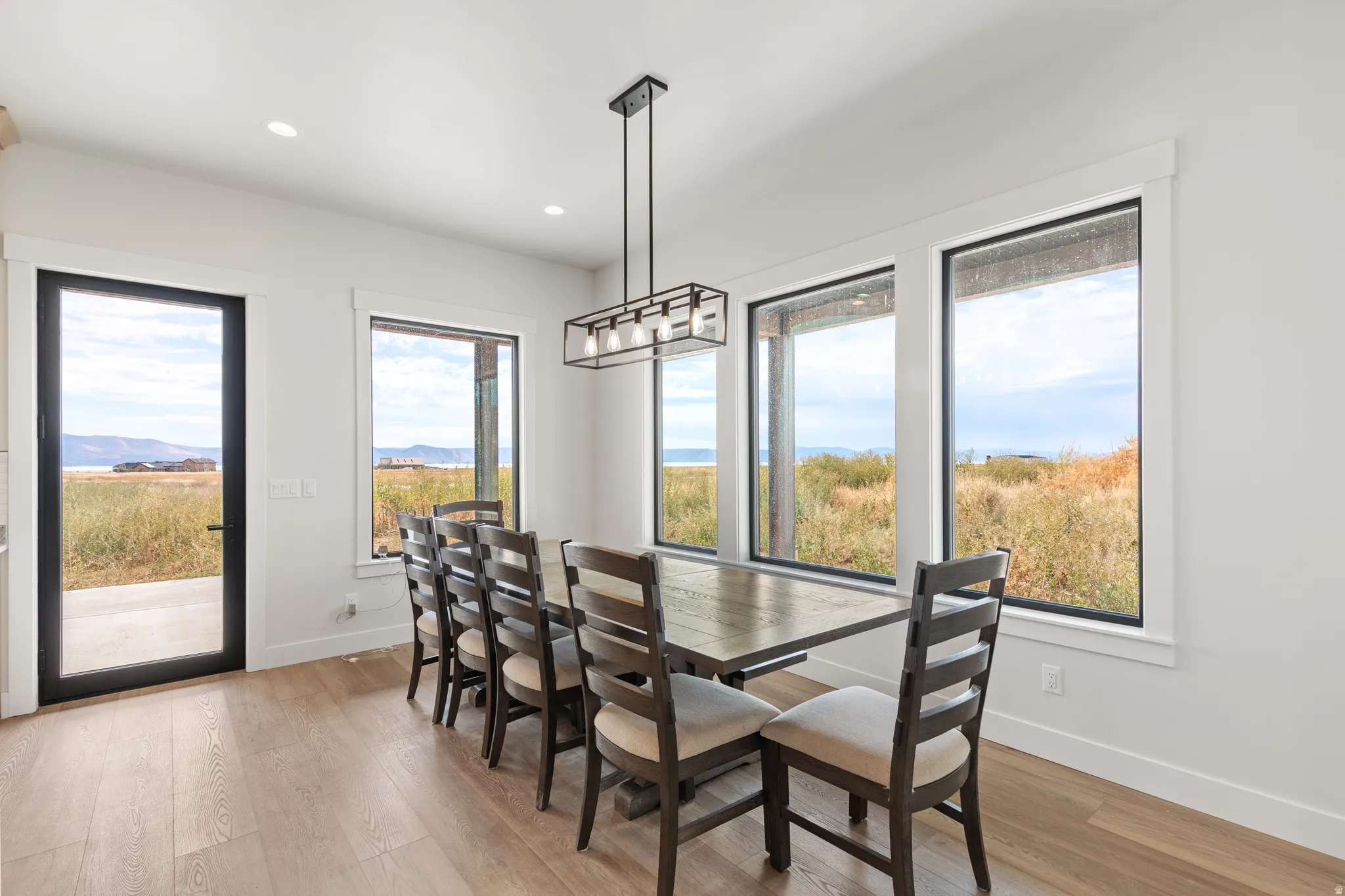 Wood-finish flooring, a contemporary linear chandelier, and abundant natural light illuminate this space