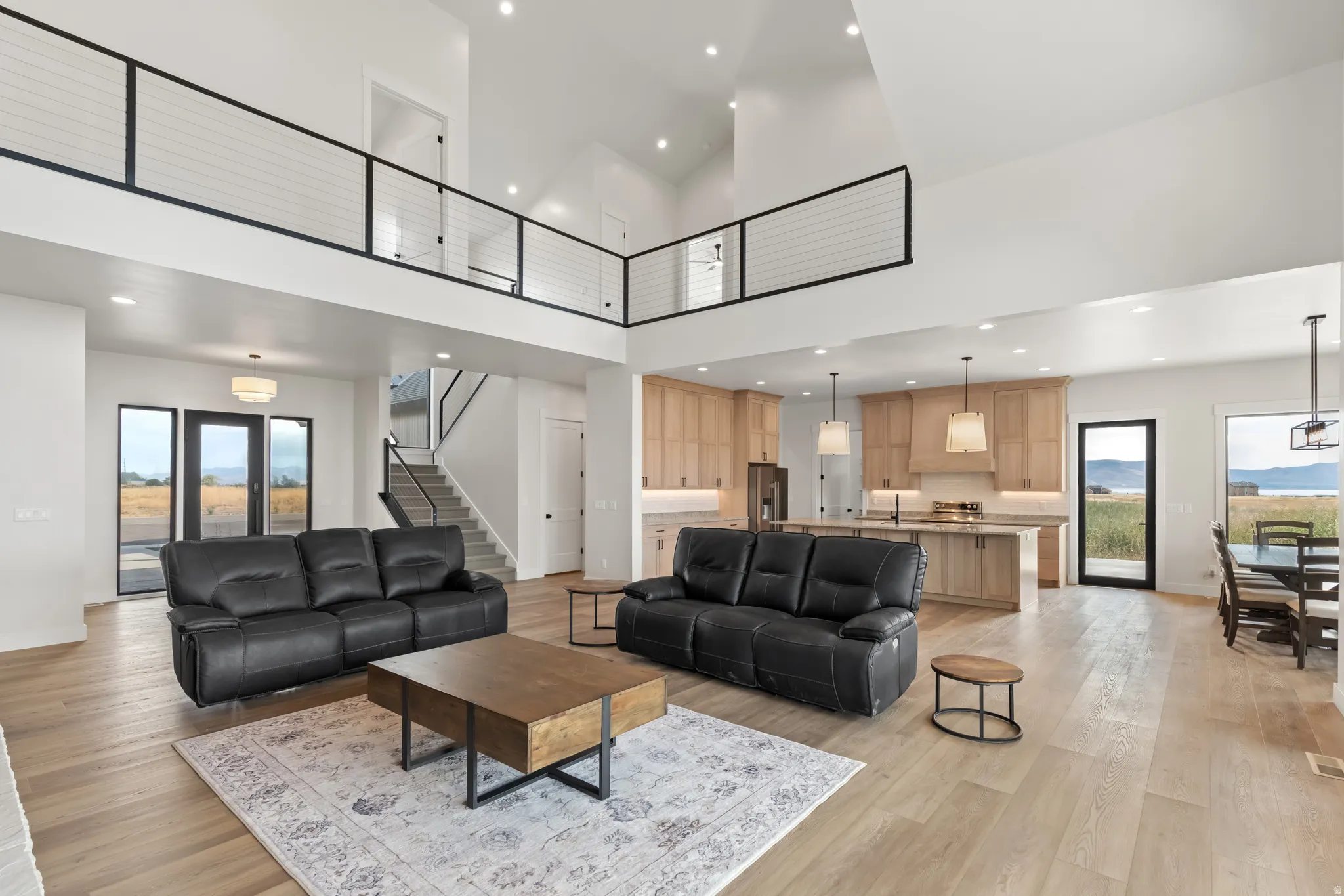 Open-concept living space featuring wood-finish flooring, a two-story vaulted ceiling, a kitchen with light wood cabinetry, and a black metal railing system