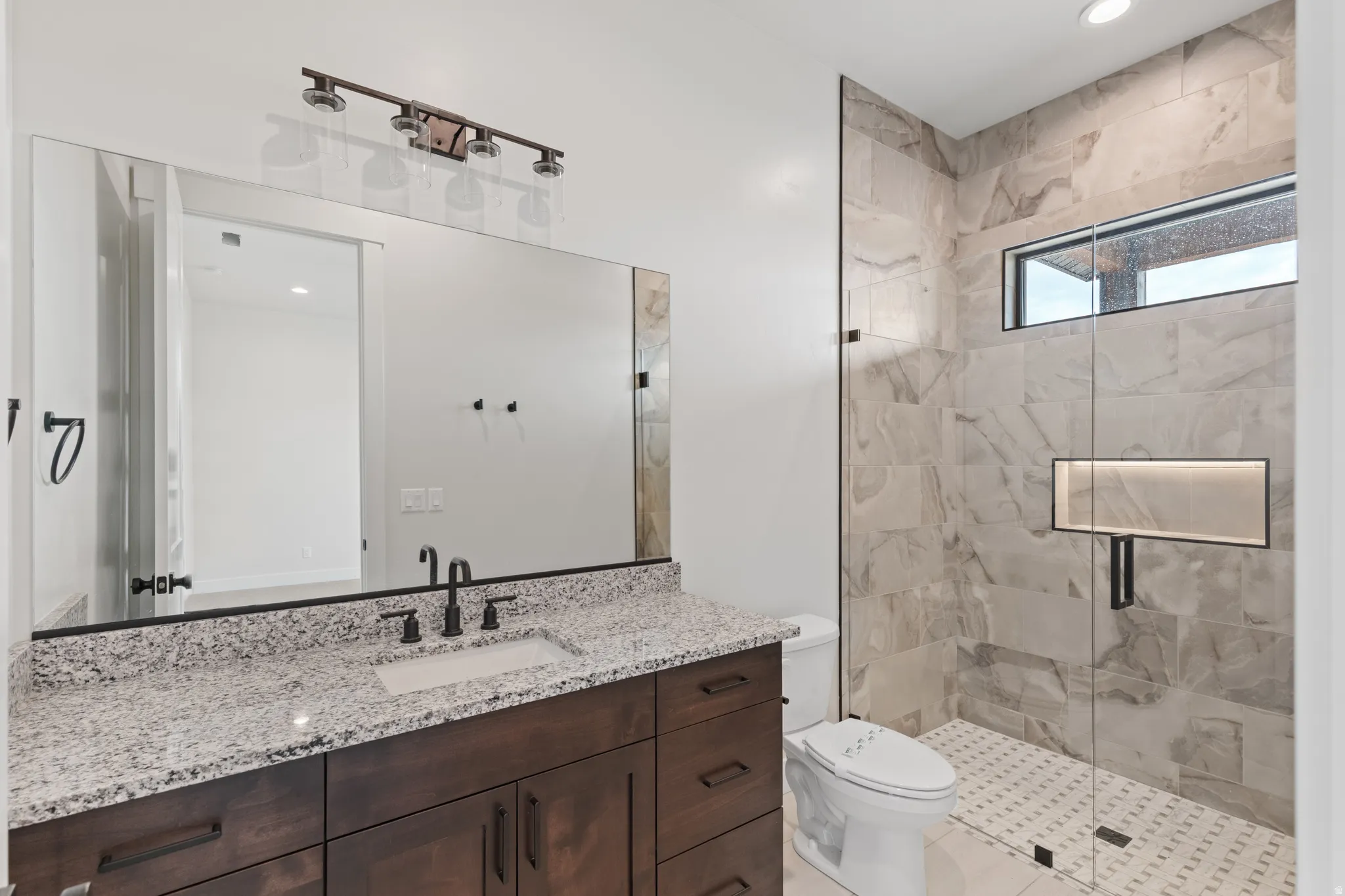Spa-inspired primary bathroom featuring a custom dark wood vanity with dual sinks, granite countertop, and polished nickel fixtures