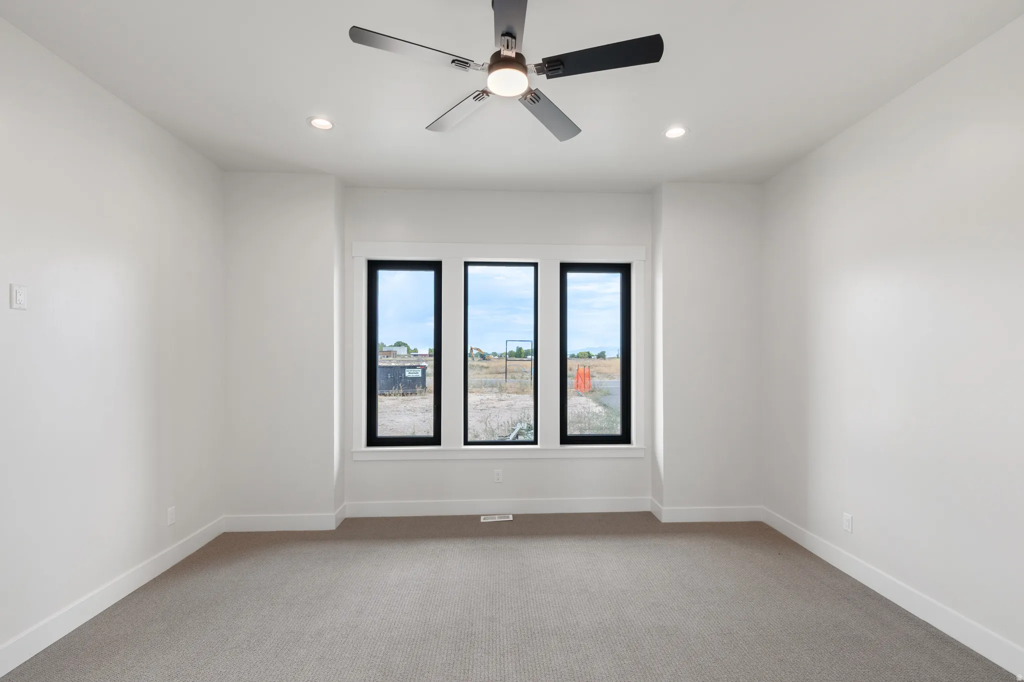 Recessed lighting, ceiling fan, white walls, gray carpet flooring, three black-framed windows