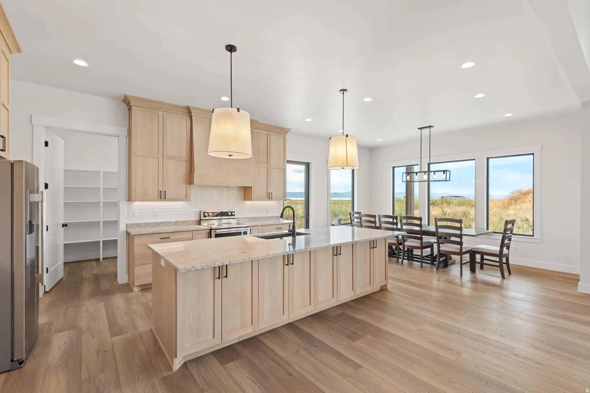 Open concept kitchen and dining area featuring wood-finish flooring, light wood cabinetry, stone countertops, and a full-size pantry