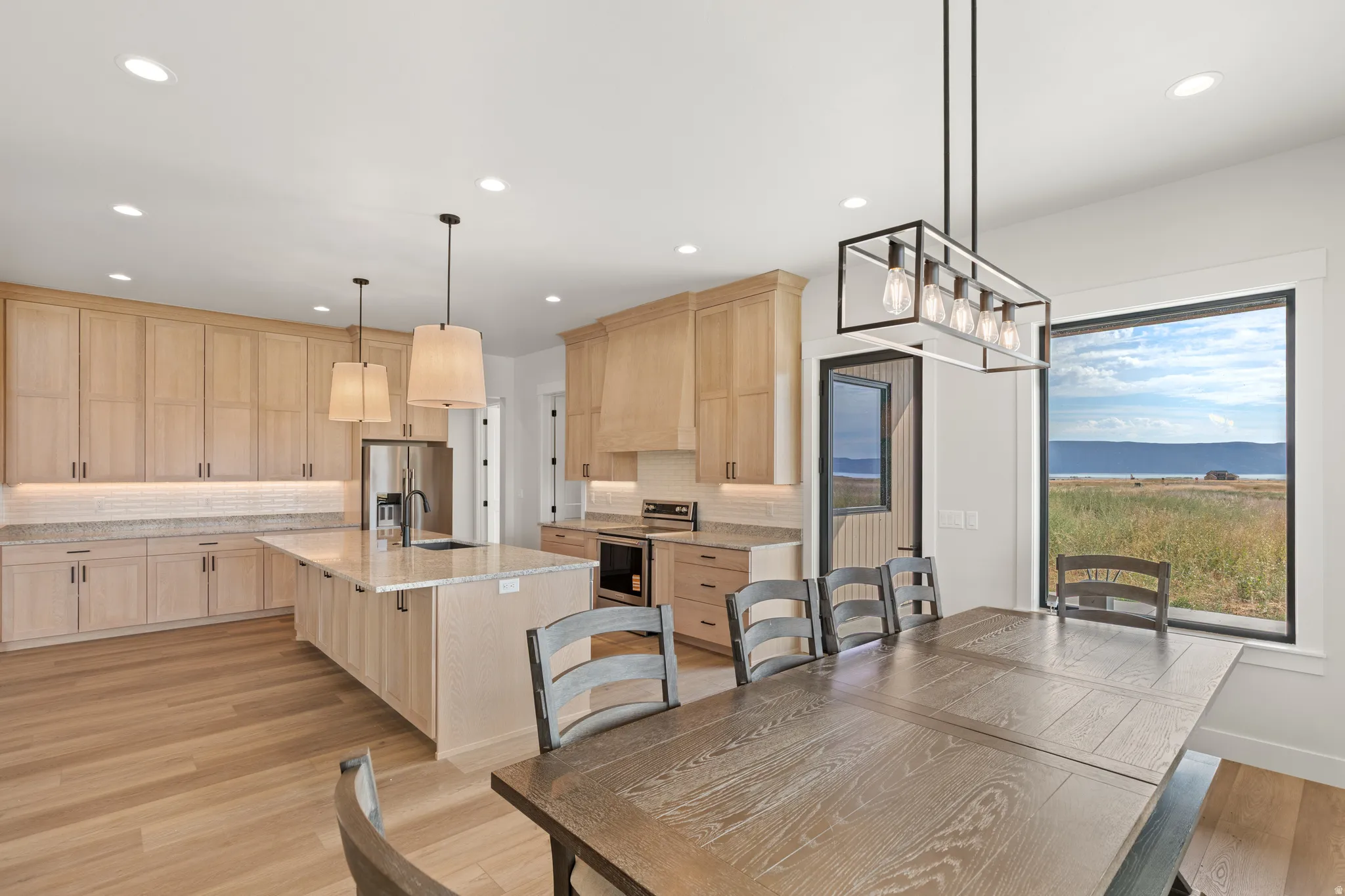 Integrated kitchen and dining area featuring light wood-finish cabinetry, granite countertops, an expansive center island, and wood-finish flooring