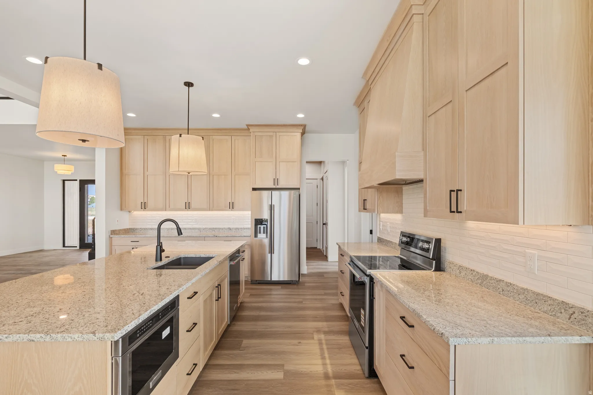 Kitchen featuring light wood-finish cabinetry, light speckled countertops, a built-in stainless steel microwave, and stainless steel appliances