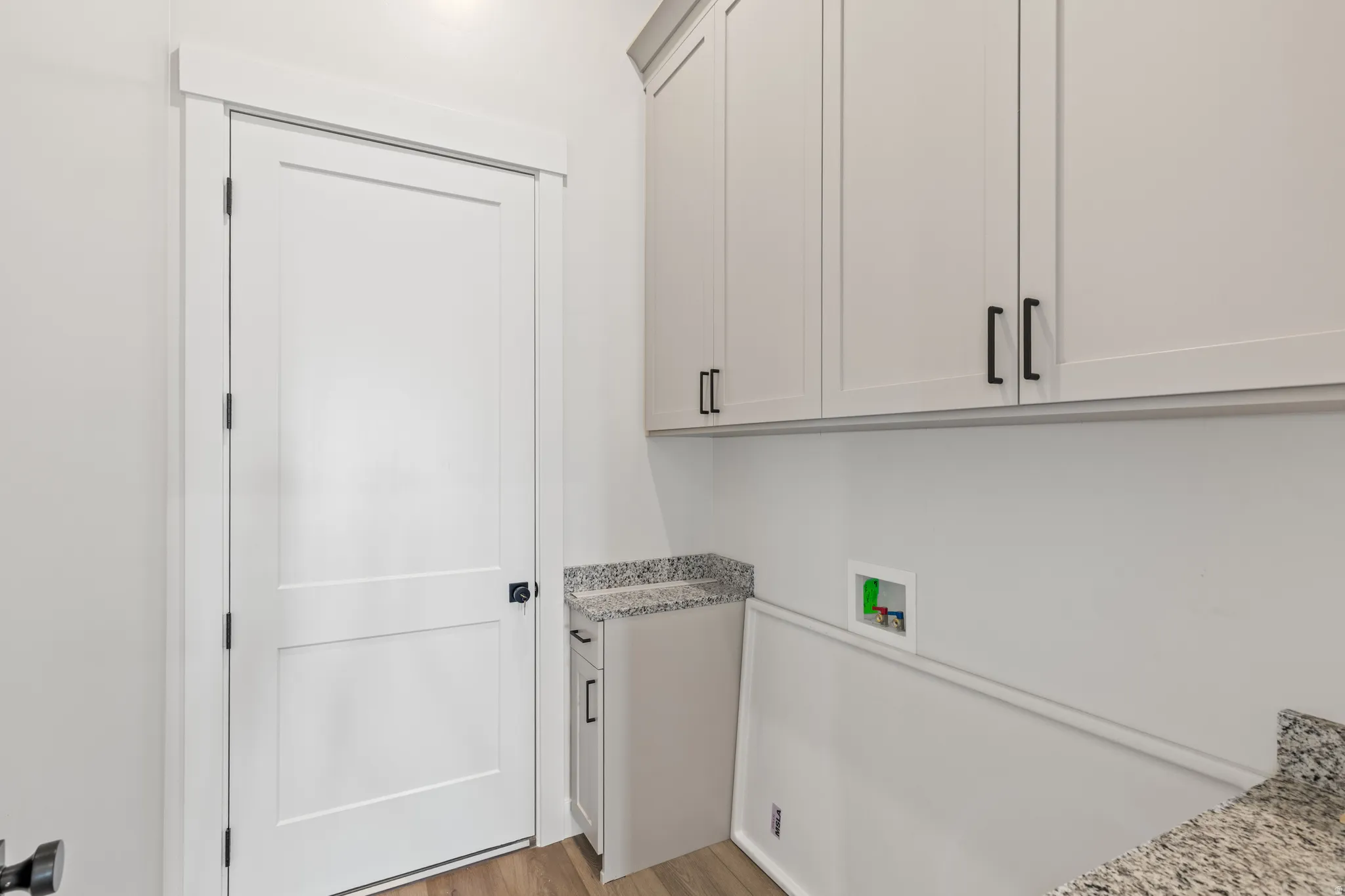 White shaker-style cabinetry with black hardware, granite-style countertops, wood-finish flooring, and white interior door with black hardware