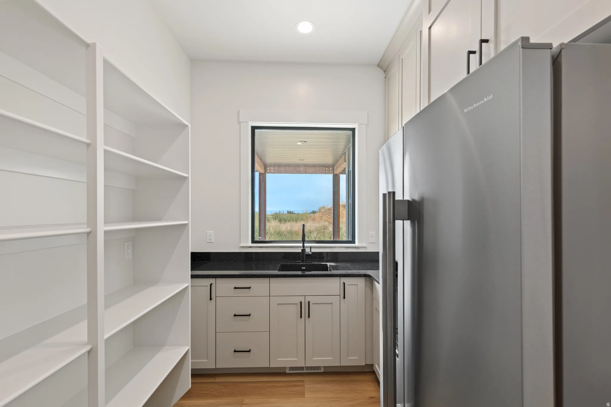 Built-in shelving, stainless steel refrigerator, dark countertop, single basin sink with a black faucet, and wood-finish flooring