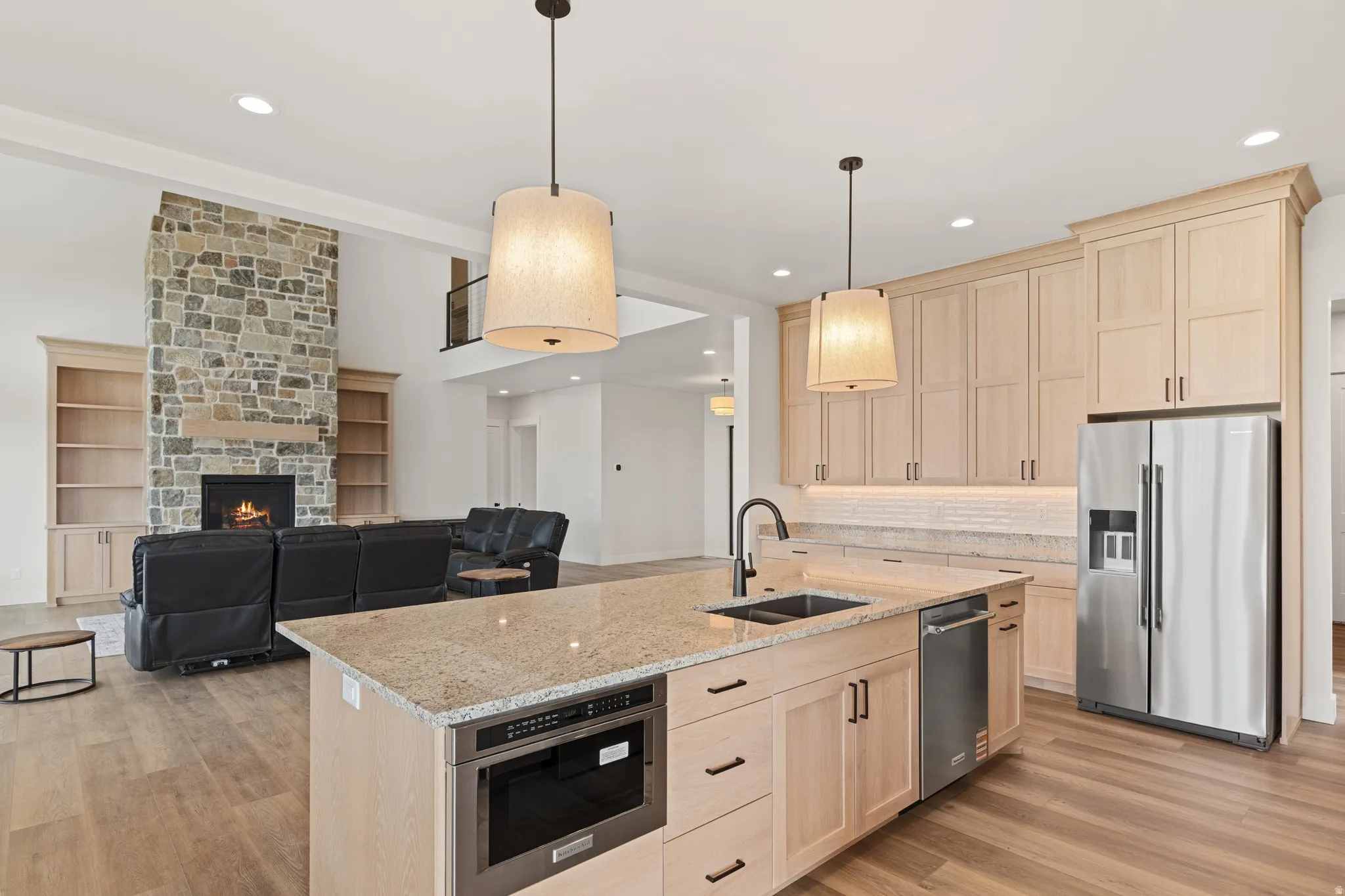 Spacious kitchen island with built-in microwave, wood-finish flooring, stone fireplace, and built-in shelving